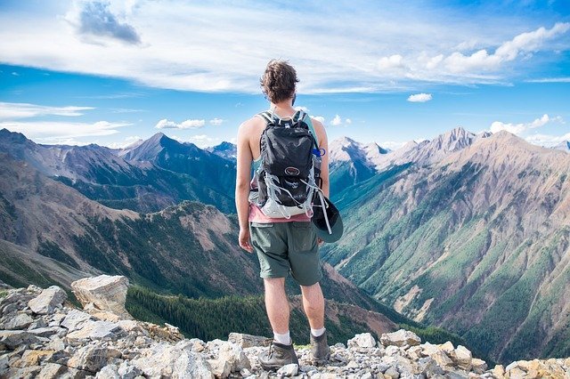 back of hiker with backpack, standing and looking out across mountain tops